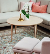 Et bilde av interiøret i hjemmet til Nina på Vitigrend. Hun har et mønstret teppe, et lyst bord i eik og en lyserosa stol. I bakgrunnen står en grå sofa med rosa puter.