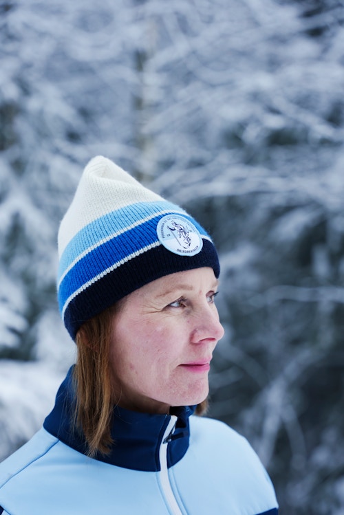 Et nærbilde av en dame som står ute i vinterlandskap. Hun har på seg skiforeningen sin lue.