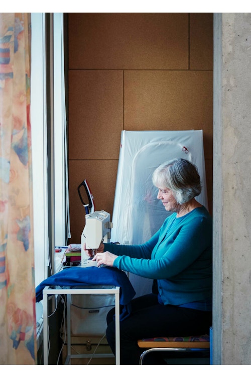 Beboer i OBOS Living Lab, Else Bakkehaug, sitter foran en symaskin og syr i blått stoff