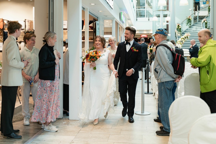 Brudeparet går igjennom kjøpesenteret og hilser på butikkansatte og andre oppmøtte.
