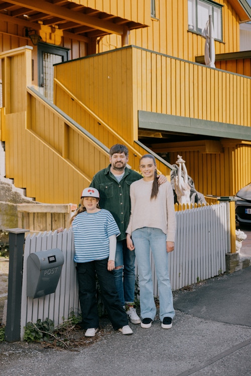 En mann og to jenter står foran et gult hus i Drøbak og poserer.