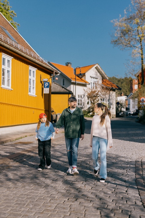Mann og to døtre går i lag i Drøbak. Det er sol. Skimter et gult hus.