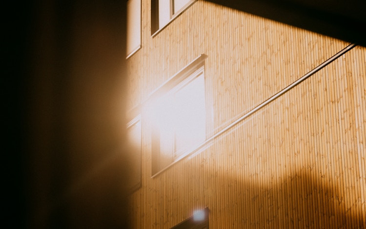 Bilde av fasade, hvor solen speiler seg i et vindu i Løren botaniske.