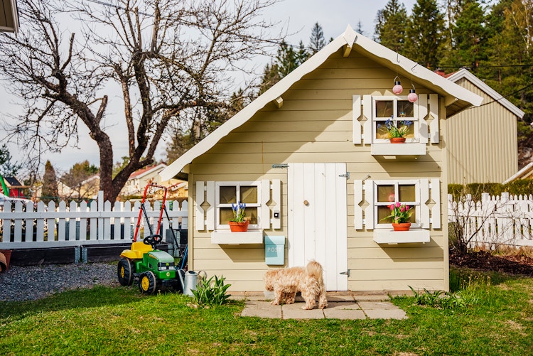 Gult lekehus i hagen med en liten hund foran døren.