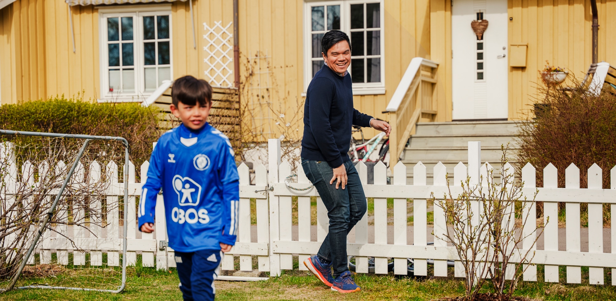 Far og sønn i familien Ødegaard Matibag spiller fotball i hagen foran gule rekkehus.