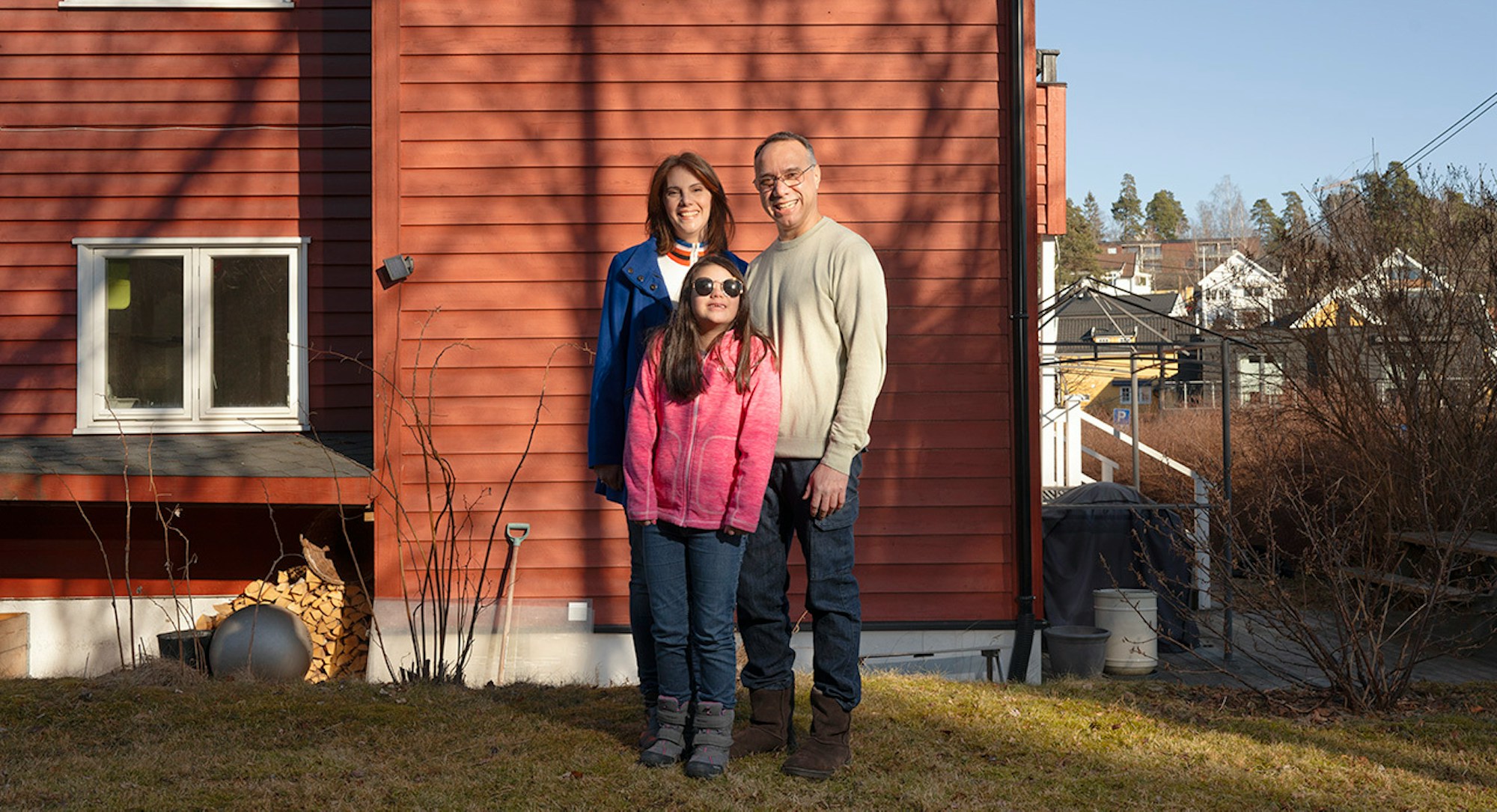 obos deleie familie på tre står foran et rødt hus