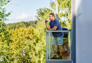 Aleksei står på balkongen sin med en kaffekopp i hånda og ser på utsikten.
