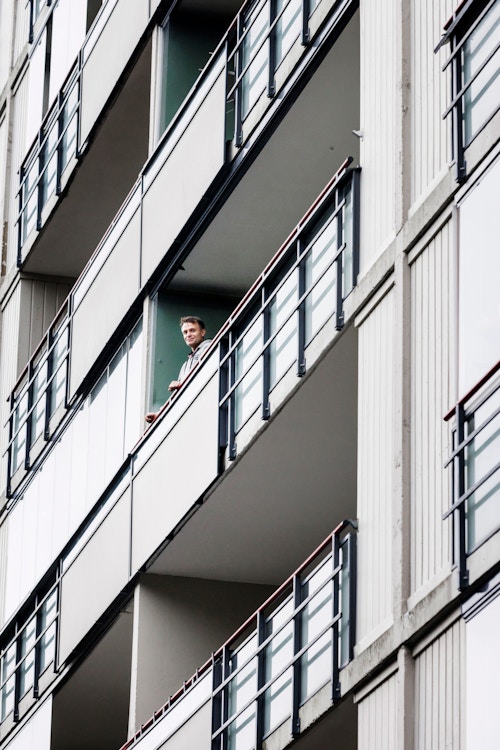 Bilde av styrelederen som står på balkongen i leiligheten sin. Bildet er tatt fra bakken.