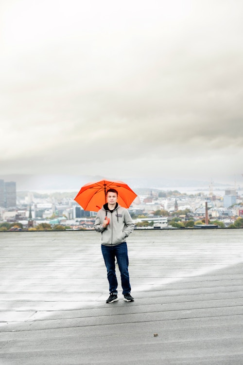 Styrelederen står på taket av borettslaget med en oransje paraply